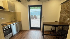 A compact kitchen with a dishwasher, oven, and a dining area with a table and chairs. - Vacation apartment Am Kreuzberg Apartment No. 3 (Nordrhein-Westfalen - Schleiden)