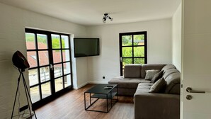 A modern living room with large windows, a flat-screen TV, a sofa, and a coffee table. - Vacation apartment Am Kreuzberg Apartment No. 3 (Nordrhein-Westfalen - Schleiden)