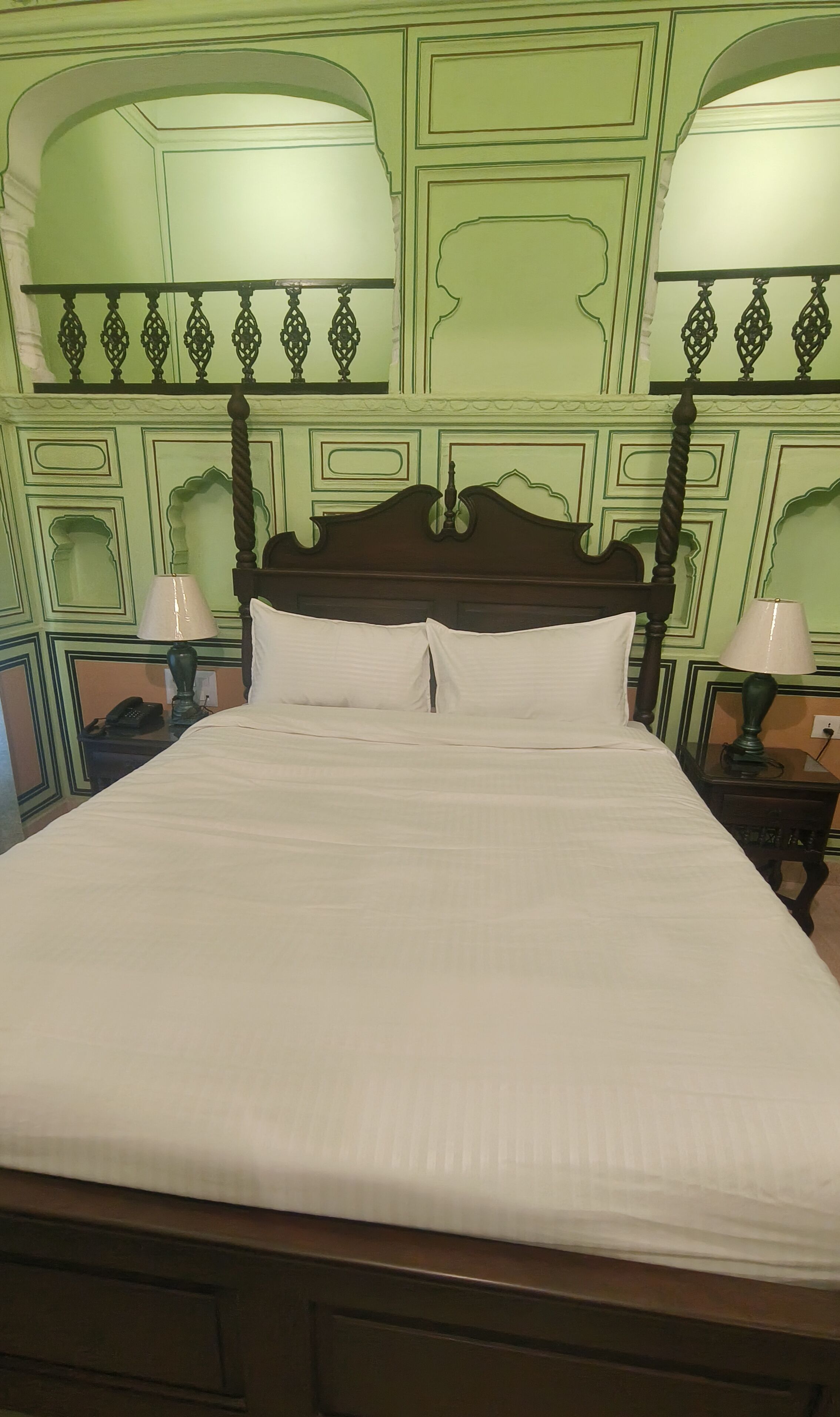 Una cama bien hecha con tablero de madera, dos mesitas de noche con lámparas y paredes cubiertas de paneles verdes.
