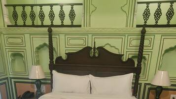 Una cama bien hecha con tablero de madera, dos mesitas de noche con lámparas y paredes cubiertas de paneles verdes.