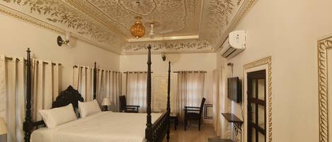 A four-poster bed with a dark wooden frame and white linens, a chandelier, and a television on the wall.