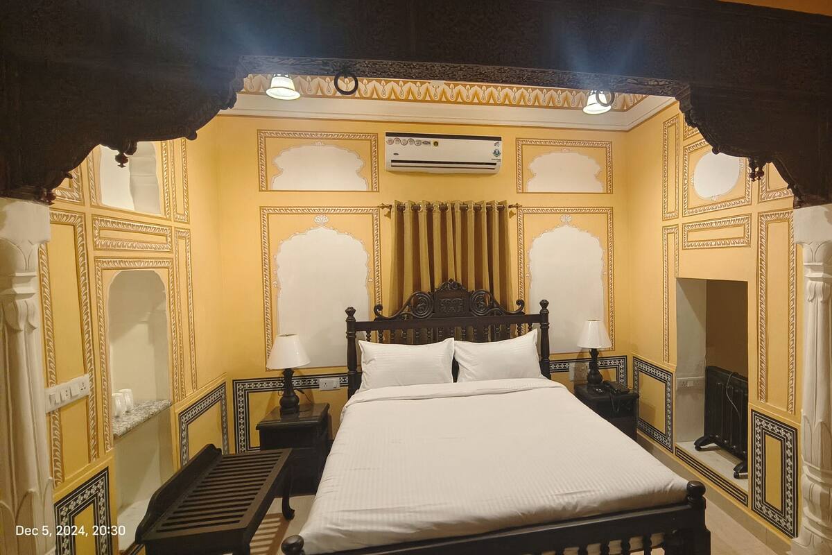 A traditional room with a bed, a nightstand, a lamp, and an air conditioning unit.