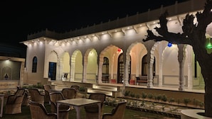 A traditional building with arched windows and a covered outdoor seating area with wicker furniture. - HOTEL MANDAWA VILAS (Jhunjhunu)