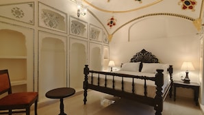 A bedroom with a bed, a chair, a nightstand, and decorative wall panels. - HOTEL MANDAWA VILAS (Jhunjhunu)