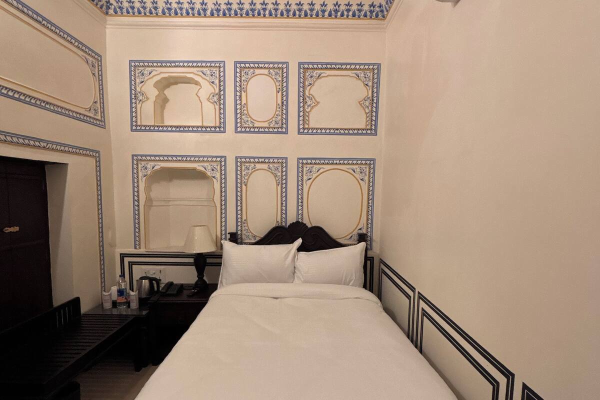 A hotel room with a large bed, a nightstand, a desk, and a chair.