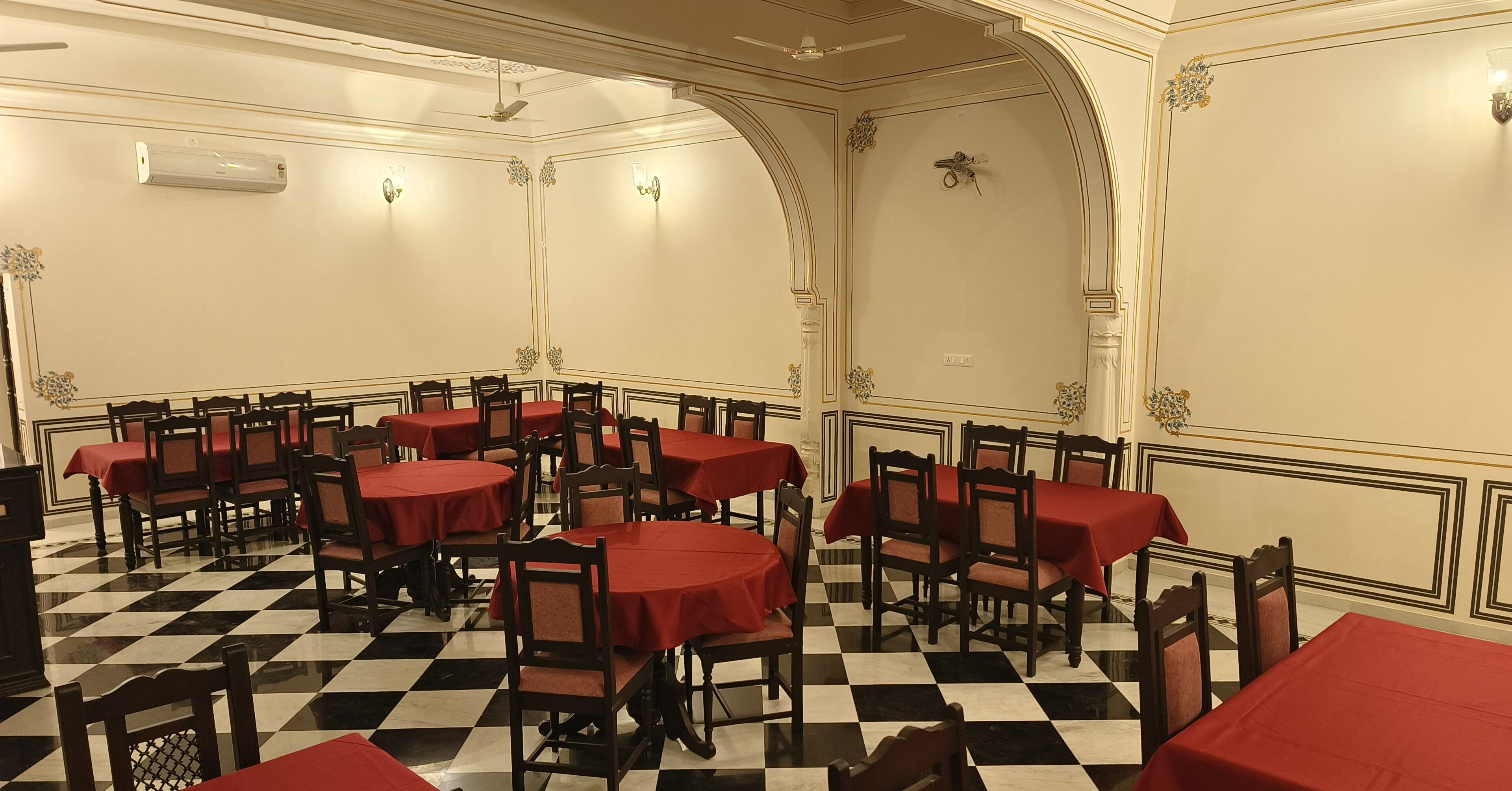 A dining area with round tables and chairs, a checkered floor, and cream-colored walls with decorative moldings.
