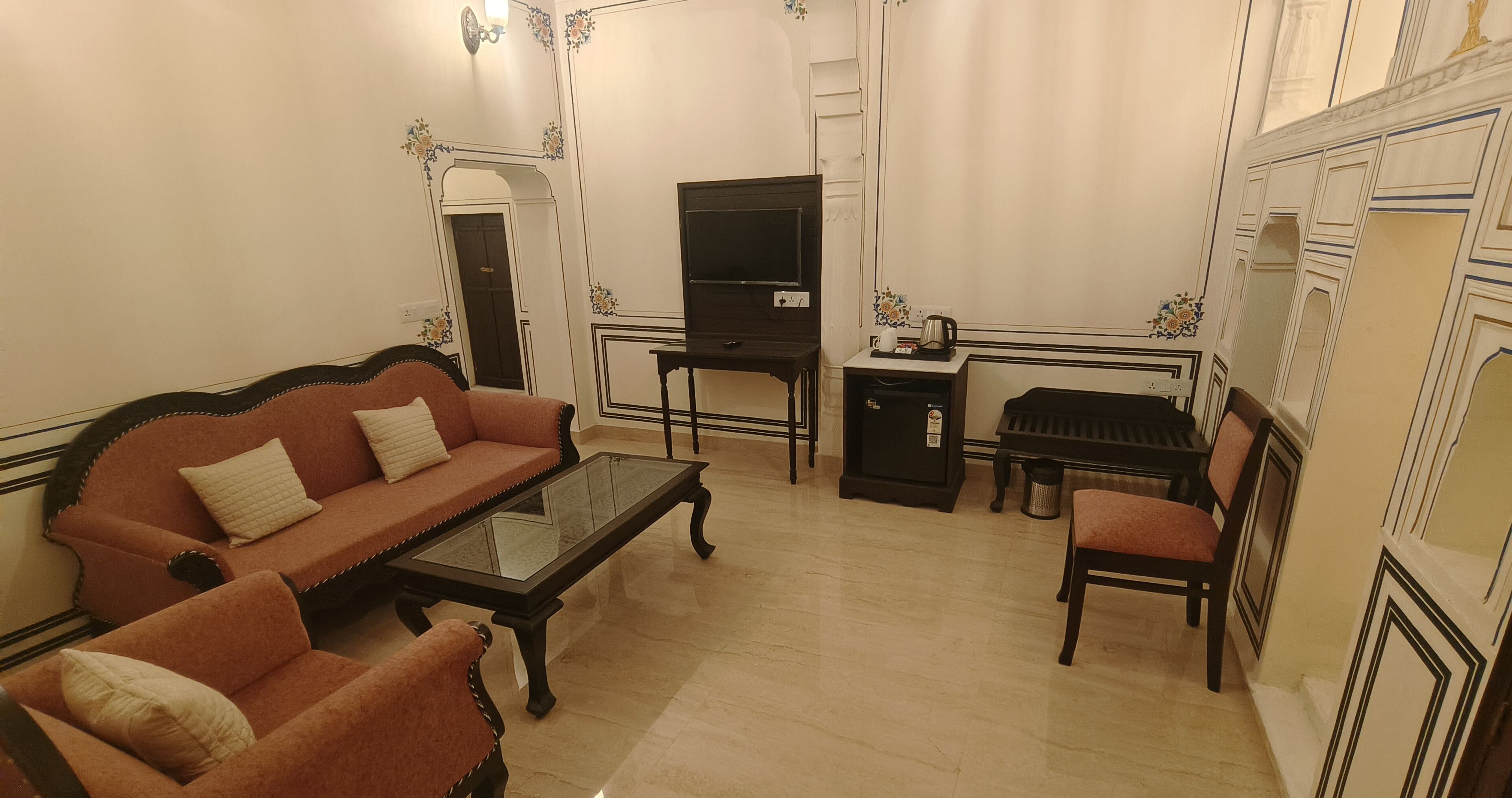 Un salon comprenant un canapé, une table basse, un téléviseur, un piano et une petite table avec une bouilloire.