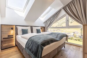 A bedroom with a large bed, skylight windows, and a view of a town. - Cosy apartment in Rauris (Rauris)