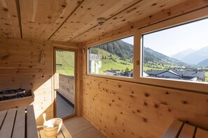 A wooden cabin with a large window offering a view of a green valley and mountains. - Cosy apartment in Rauris (Rauris)