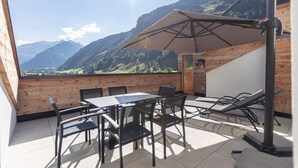 A terrace with a table and chairs, a sun umbrella, and a view of mountains.