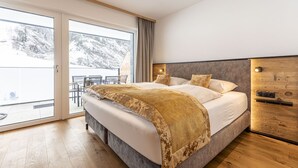 A modern bedroom with a large bed, a wooden headboard, and a sliding glass door leading to a balcony with a view of snow-covered mountains. - Spacious apartment with balcony (Rauris)