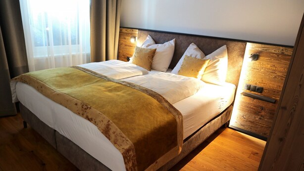 A large bed with a wooden headboard, white bedding, and a yellow throw blanket.