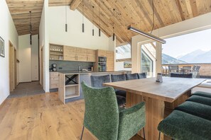 A modern kitchen with wooden cabinets and a dining area with green upholstered chairs.
