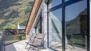 Un bâtiment moderne doté de grandes fenêtres en verre et d’un balcon avec deux fauteuils de relaxation.