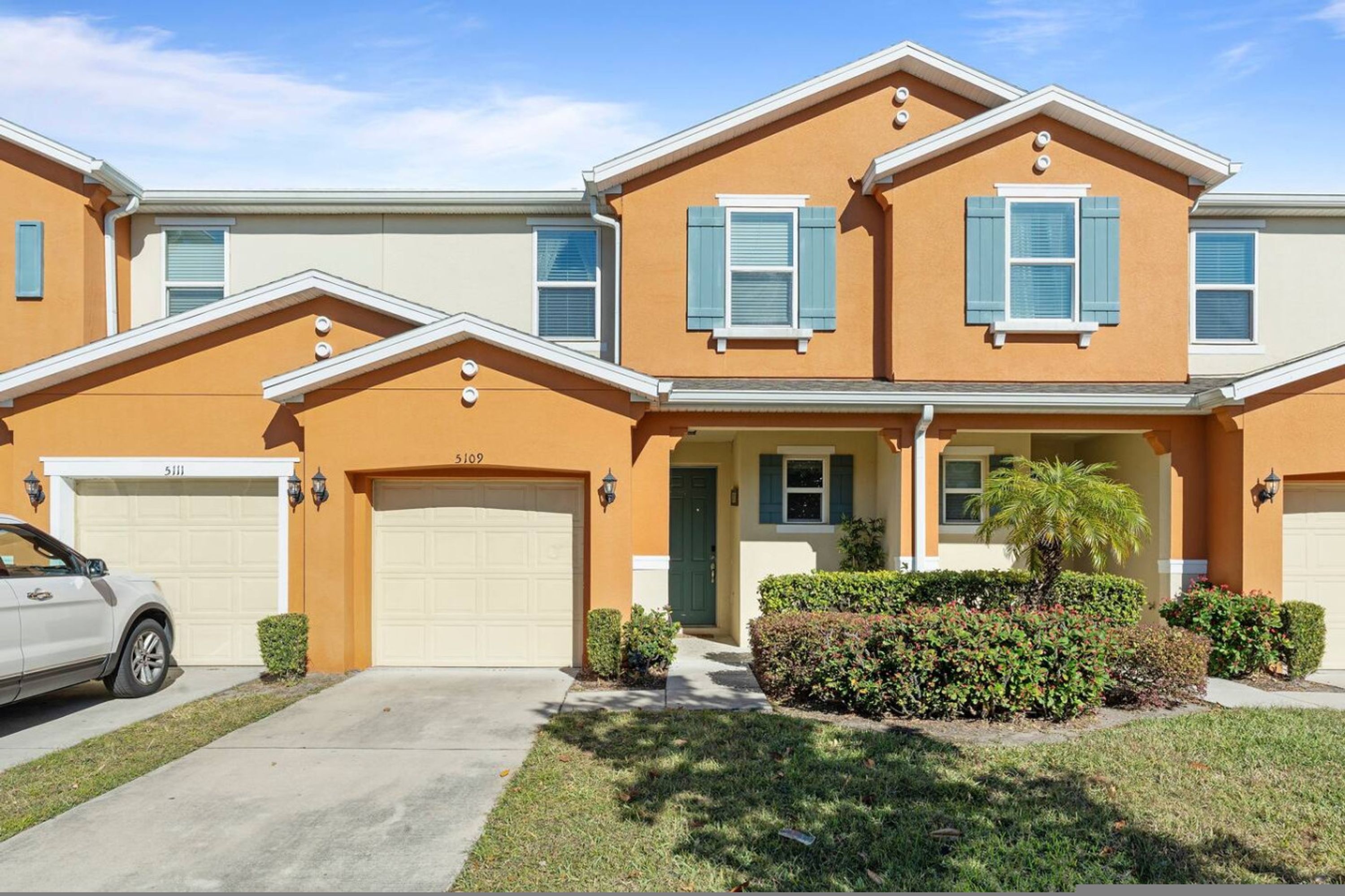 A two-story residential building with a garage, a front entrance, and a well-maintained lawn.