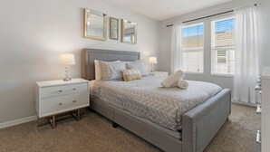 Une chambre à coucher avec un lit, des tables de chevet, un ventilateur de plafond et une fenêtre avec des stores.