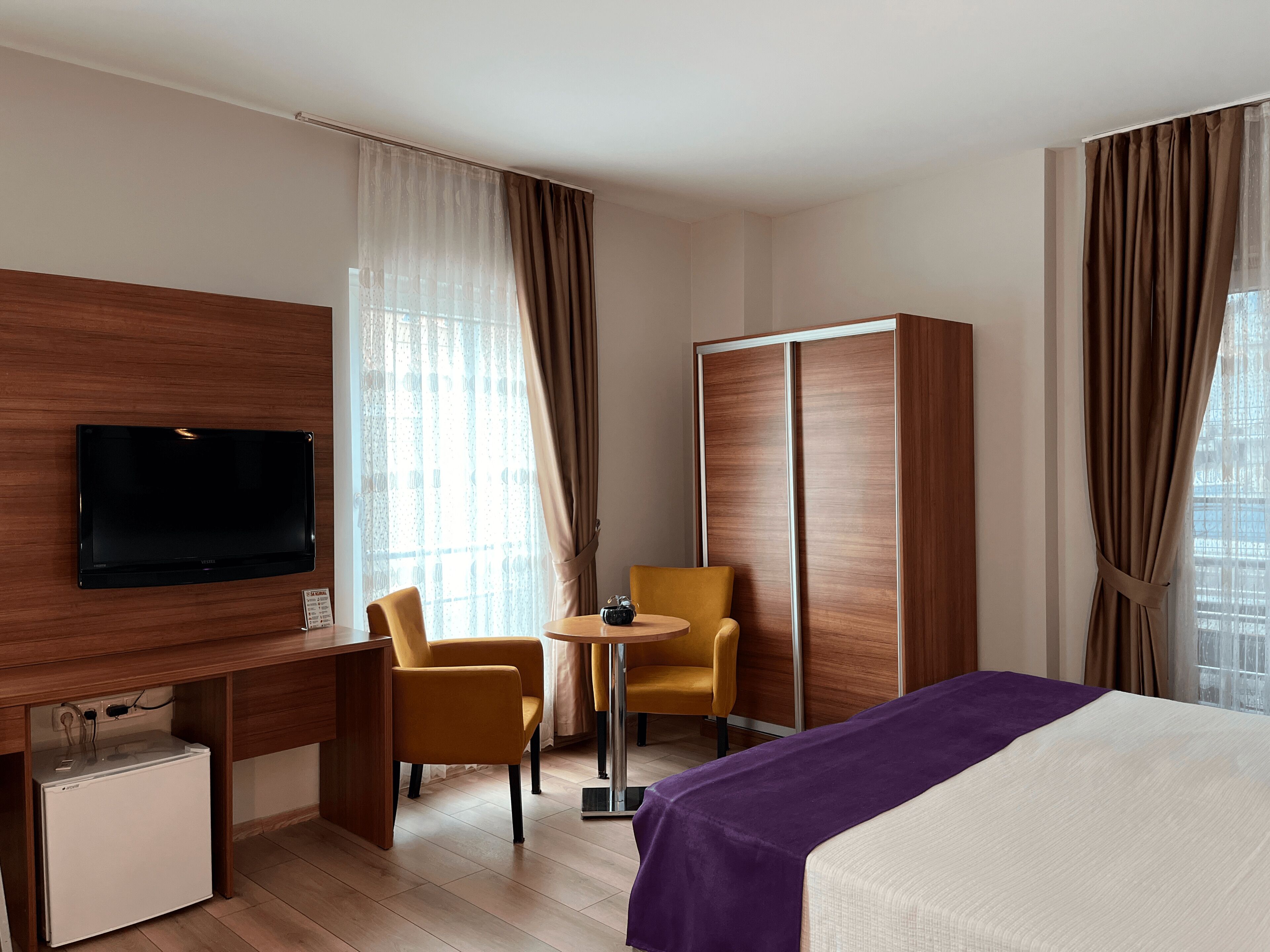 A hotel room with a bed, a desk with a television, two chairs, a small table, and a wardrobe.