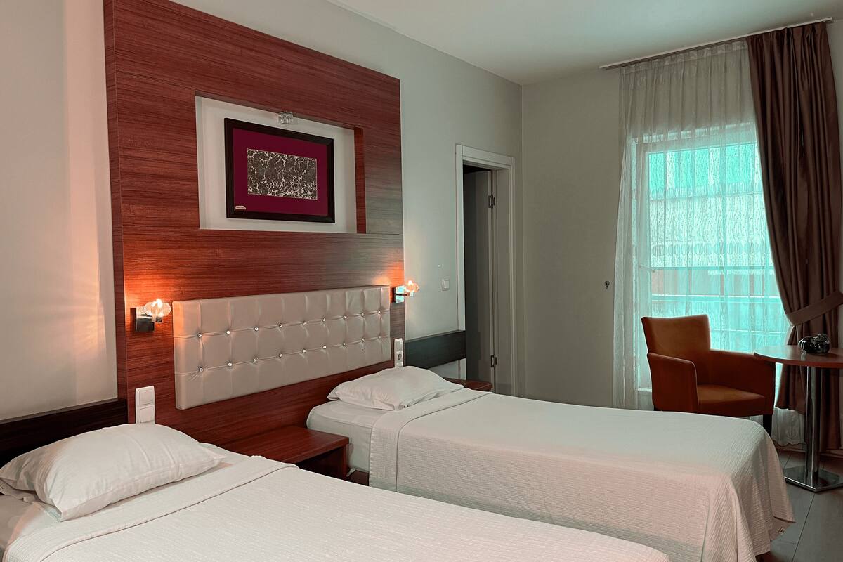 Une chambre d’hôtel avec deux lits simples, une tête de lit en bois, un tableau encadré, une petite table et une chaise.