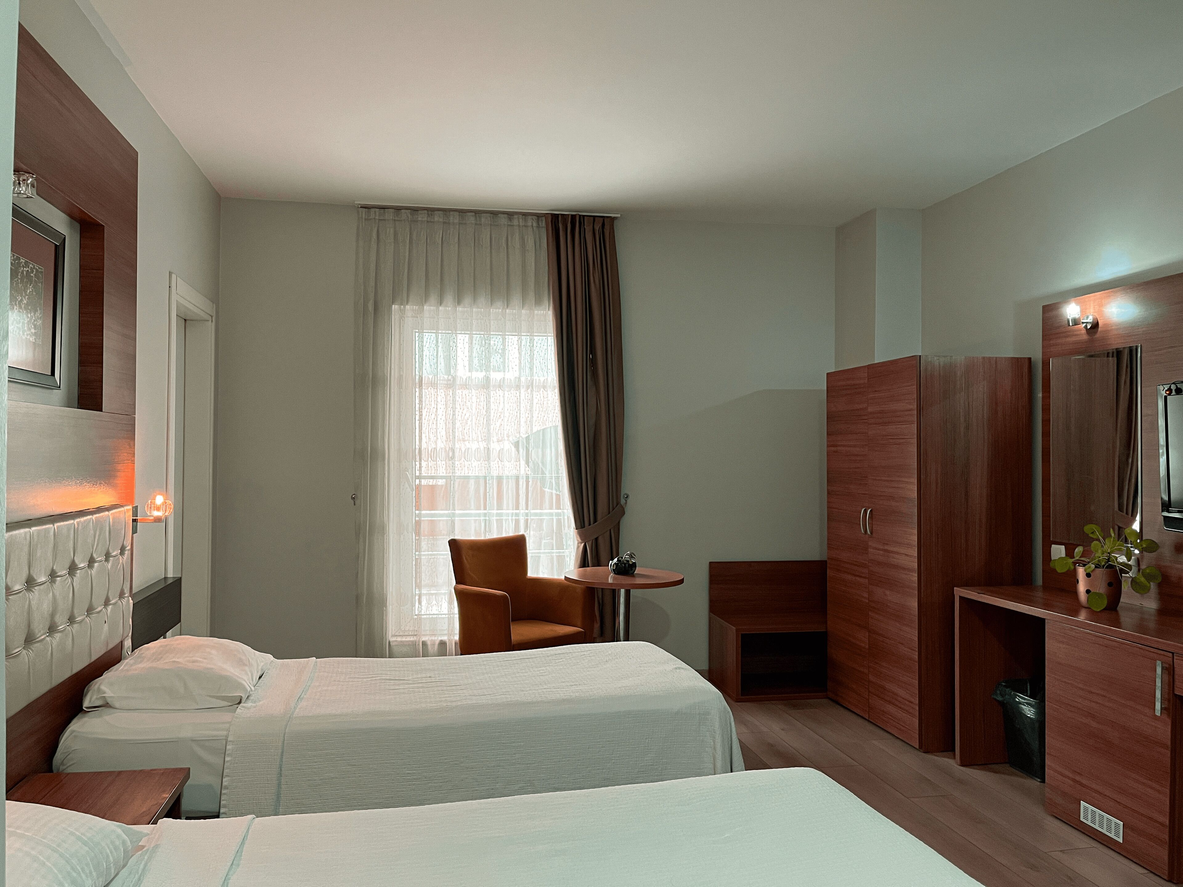 Habitación de hotel con dos camas, una mesita, una silla, un armario y una ventana con cortinas.