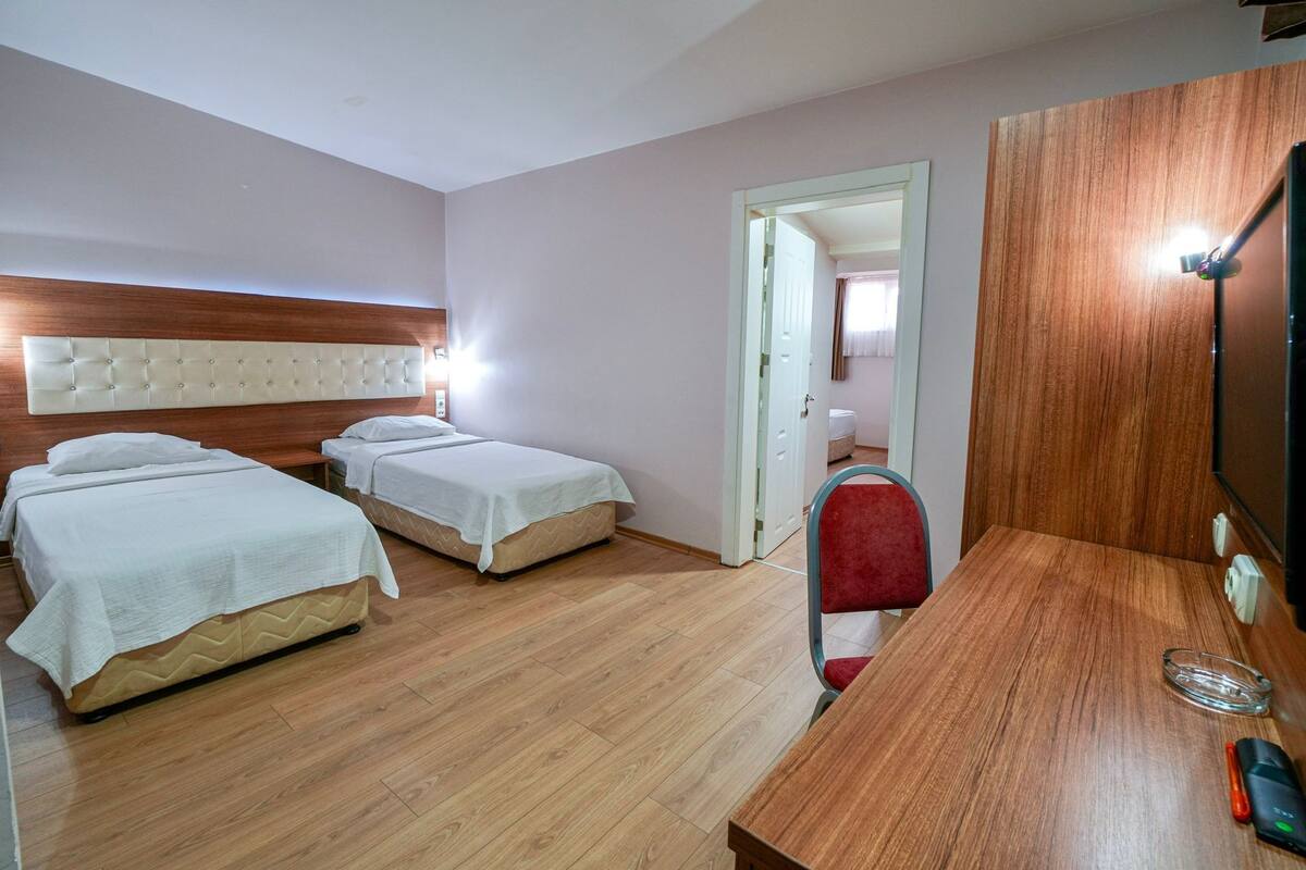 Une chambre d’hôtel avec deux lits, une tête de lit en bois, un bureau avec une chaise et un téléviseur.