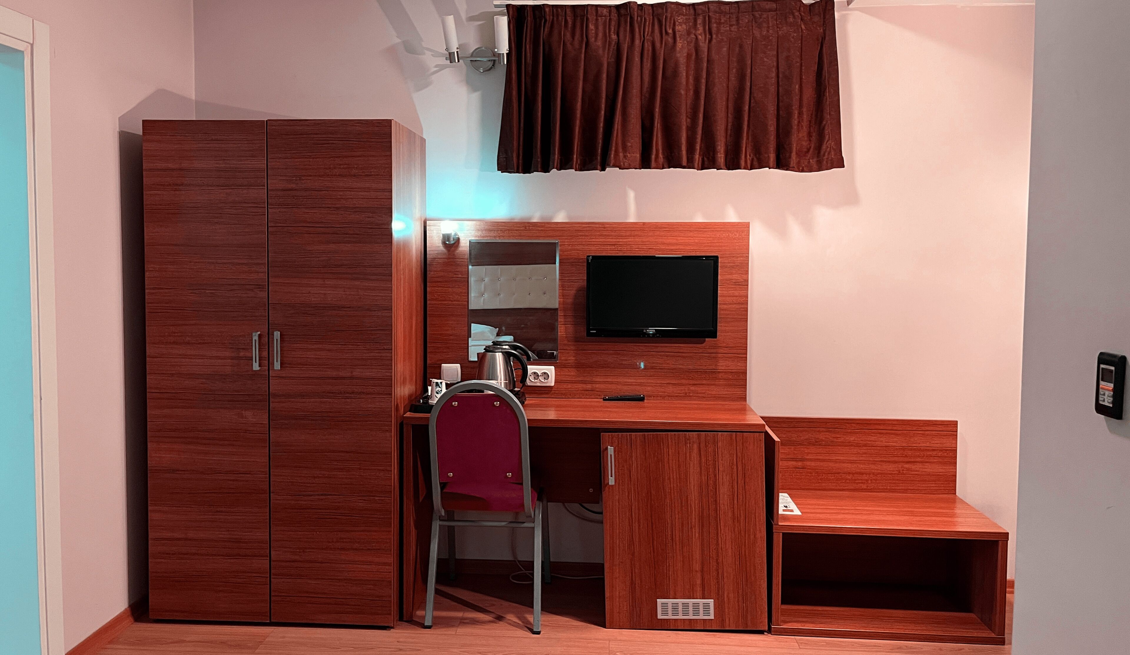 A compact room with a wardrobe, a desk with a chair, a television, and a small step.