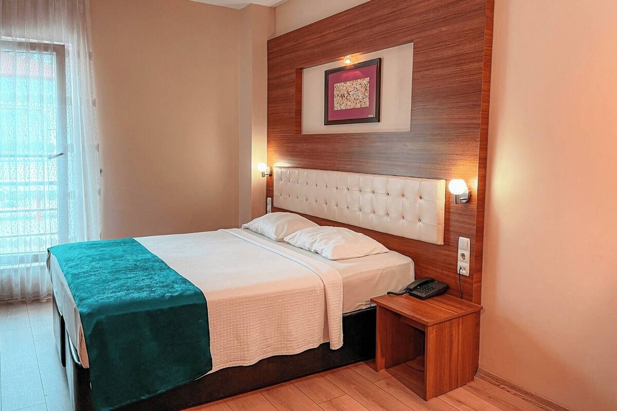 Une chambre d’hôtel bien rangée, avec un grand lit, une table de chevet avec un téléphone et un cadre photo accroché au mur.