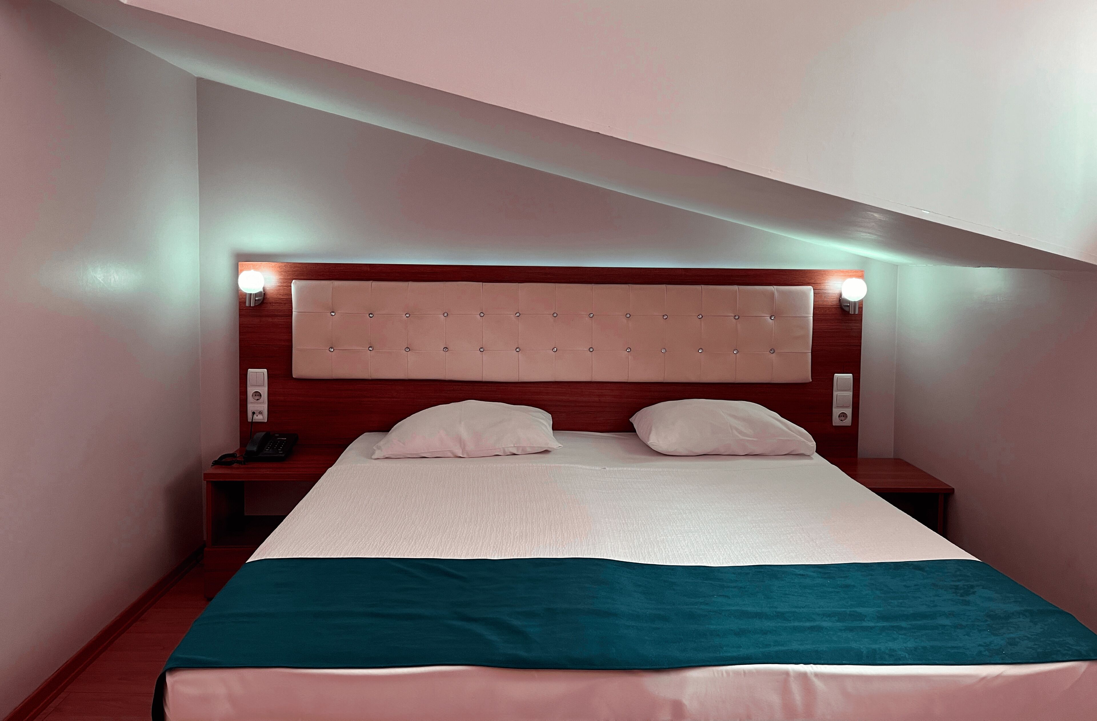 A hotel room with a bed, bedside tables, and a headboard with wall-mounted lights.