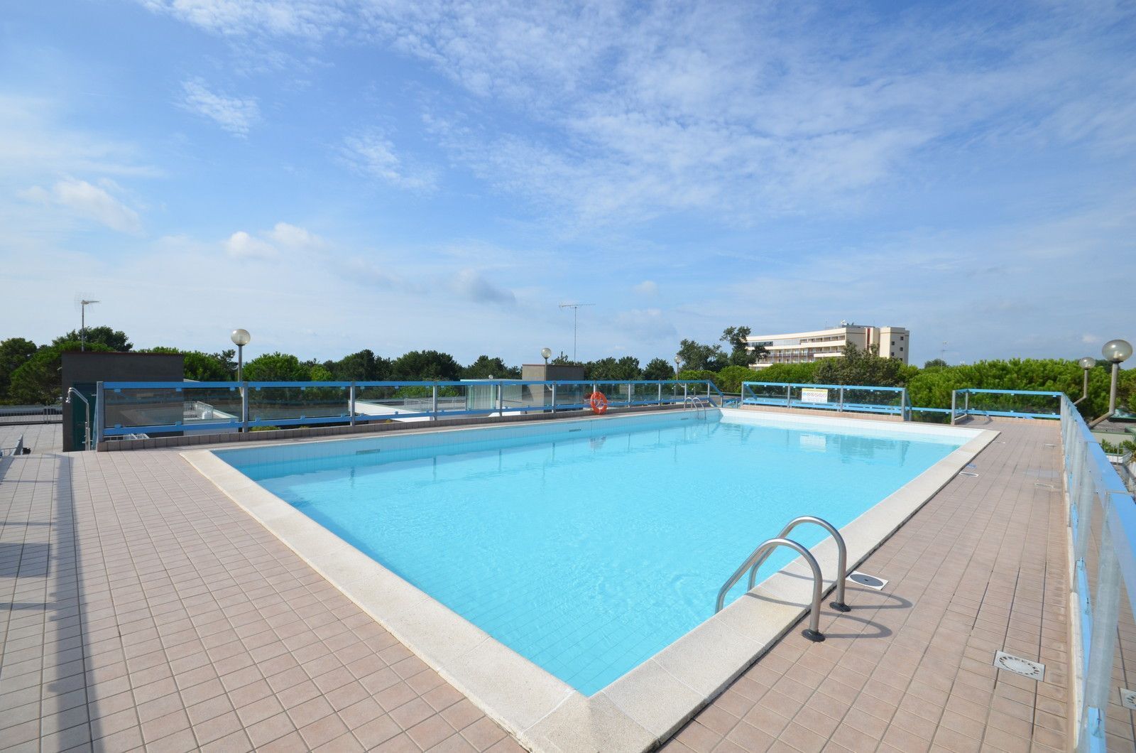 A rectangular outdoor swimming pool with a tiled deck, metal railings, and a lifebuoy.