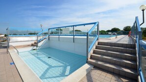 A rooftop swimming pool with clear blue water, a glass enclosure, and a set of stairs leading to the pool. - Modern apartment with garden, 100m from the beach (Bibione)