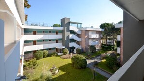 A multi-story building with balconies, a courtyard with a fountain, and a clear sky. - Modern apartment with garden, 100m from the beach (Bibione)