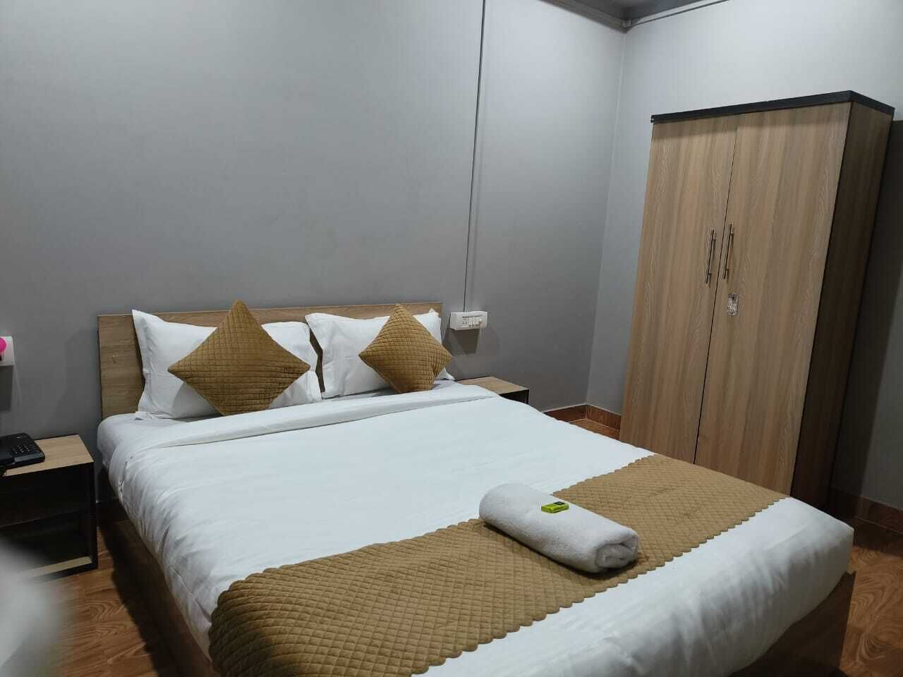 A neatly made bed with a white and brown bedspread, two pillows, and a rolled towel.