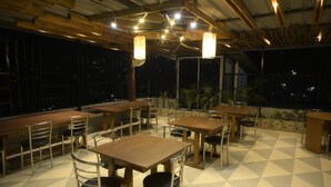 An outdoor dining area with tables and chairs, large windows, and hanging lights. - Hotel Pohor Regency Near Kamakhya Foot Bridge (Guwahati)