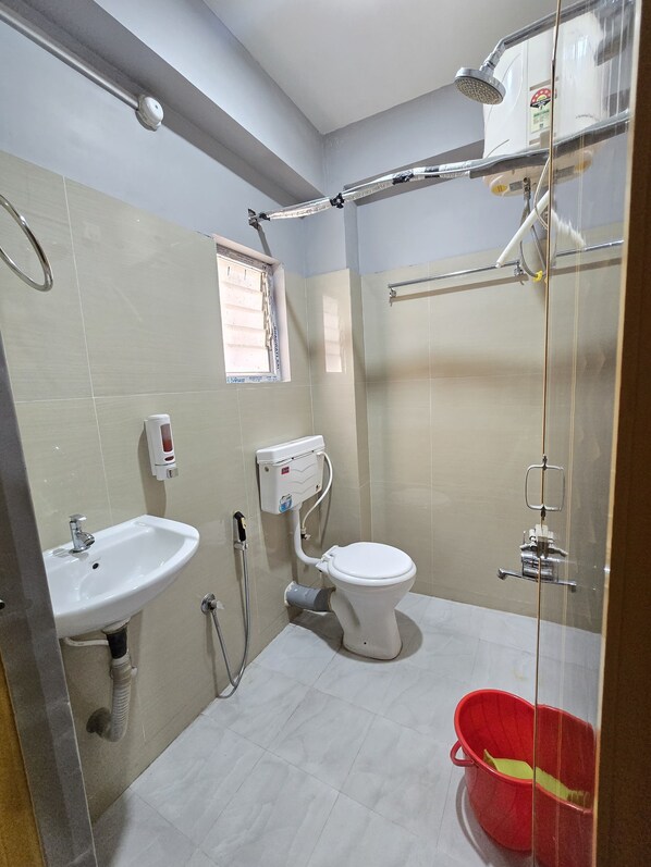 A bathroom with a sink, toilet, shower, and a red bucket. - Hotel Pohor Regency Near Kamakhya Foot Bridge (Guwahati)