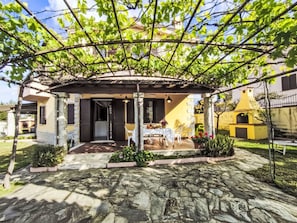 Un patio cubierto con suelo de piedra, una mesa con sillas y un edificio amarillo al fondo.