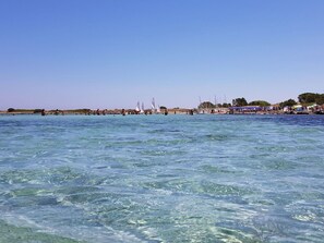 Ein Strand mit klarem, blauem Wasser, Menschen beim Schwimmen und Booten.