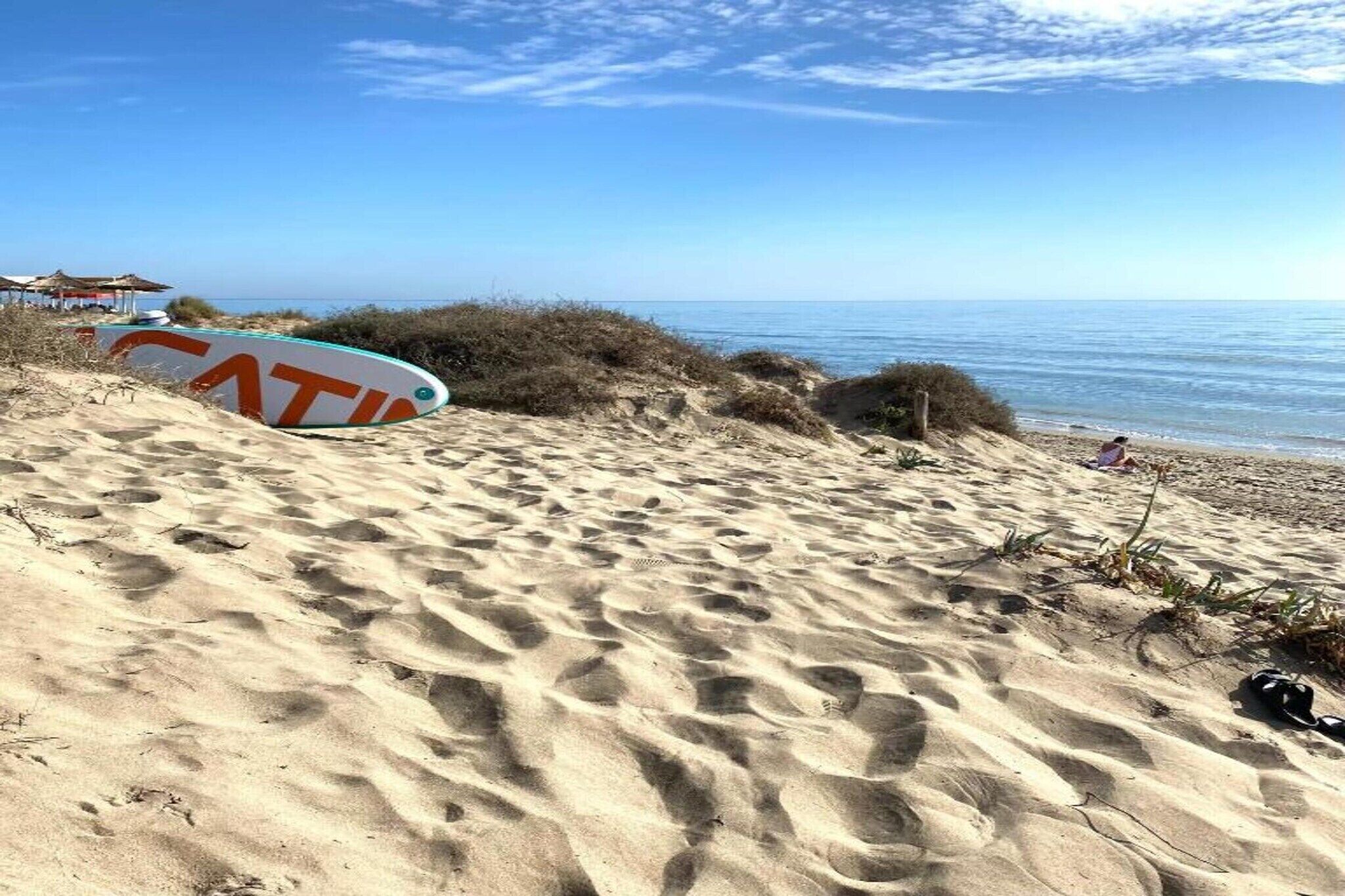 A sandy beach with footprints and a surfboard.