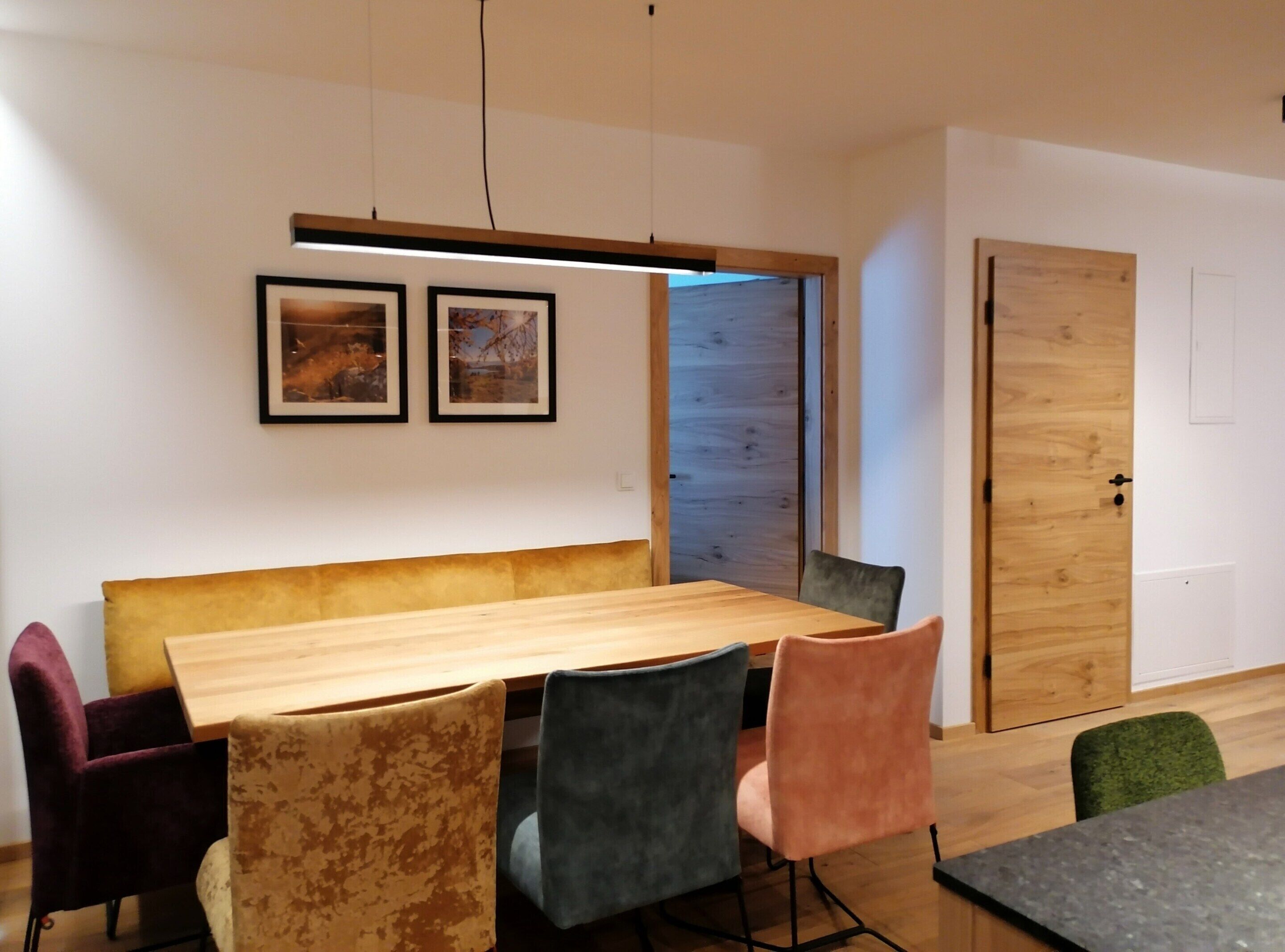 A modern meeting room with a wooden table, colorful chairs, framed pictures on the wall, and a wooden door.