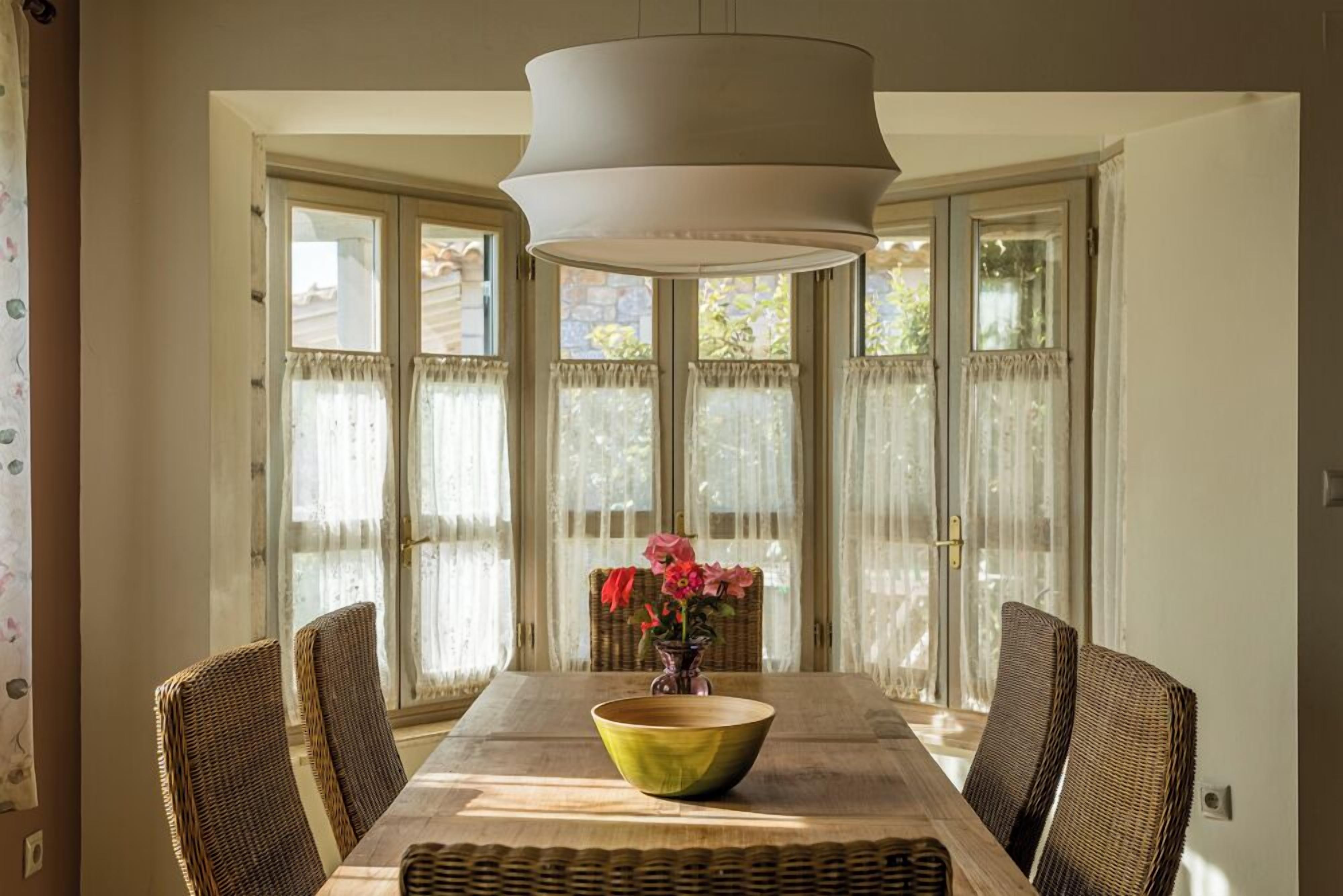 A dining area with a table, chairs, a vase with flowers, and a large hanging light fixture.