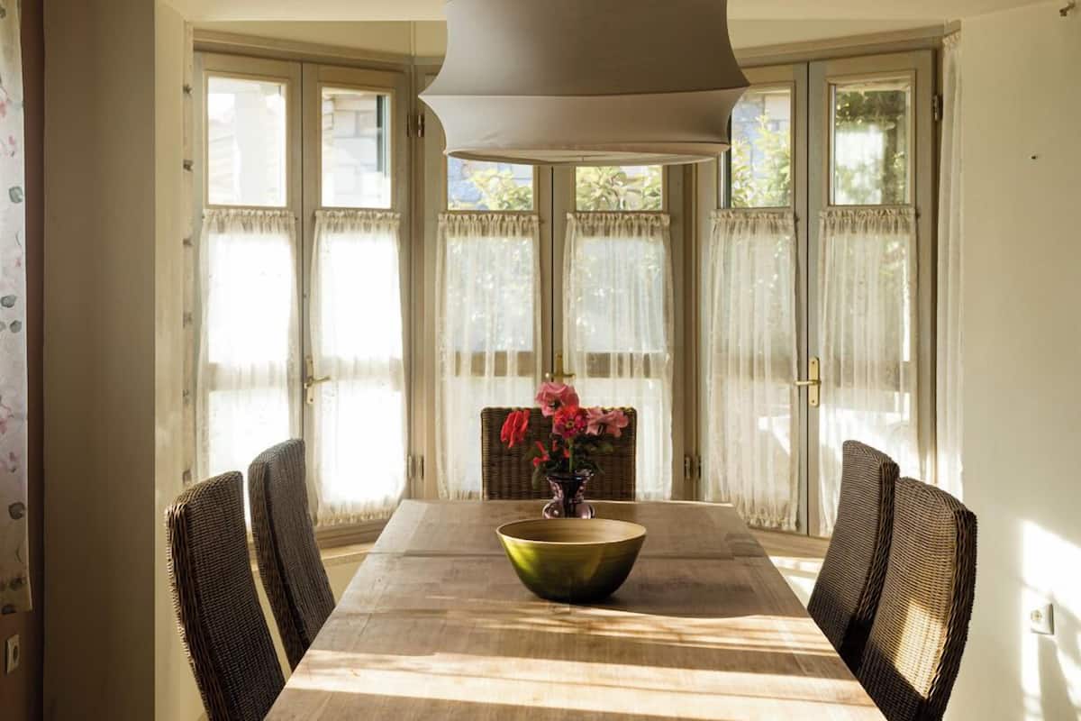 Un coin repas avec une longue table en bois, des chaises en osier et un vase rempli de fleurs.