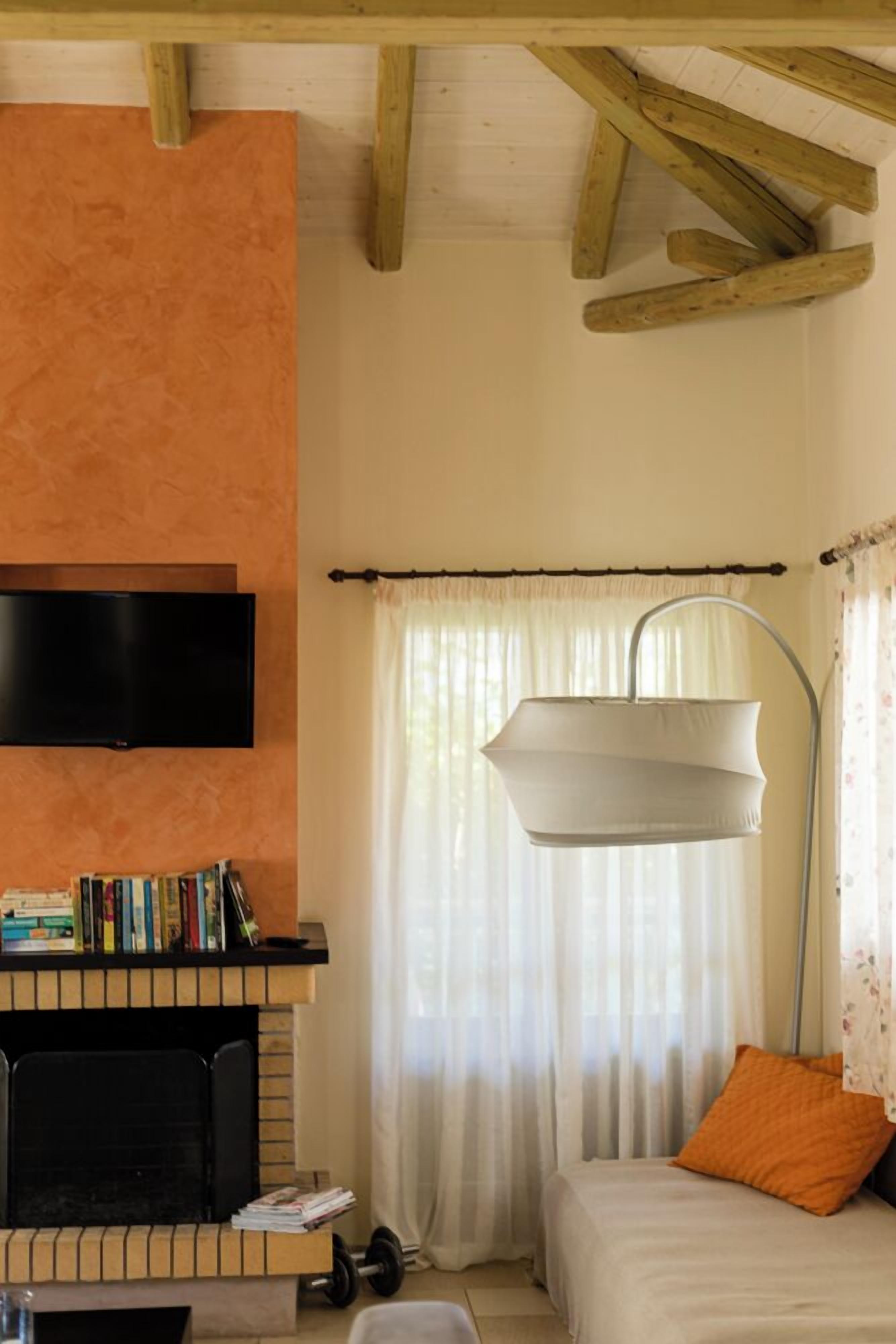 Una camera accogliente con un camino, una TV a schermo piatto, una libreria e un letto con un cuscino arancione.