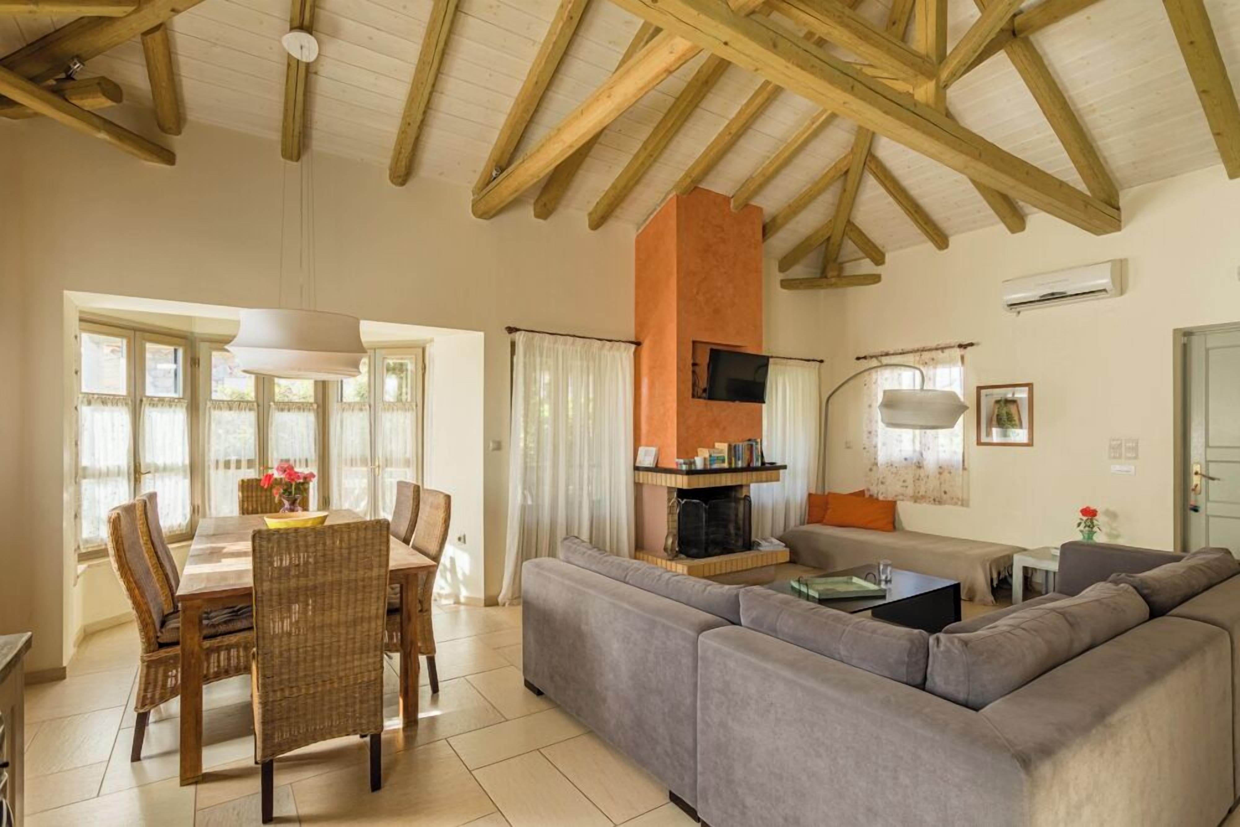 A spacious living area with a wooden ceiling, a fireplace, a sofa, and a dining table with chairs.