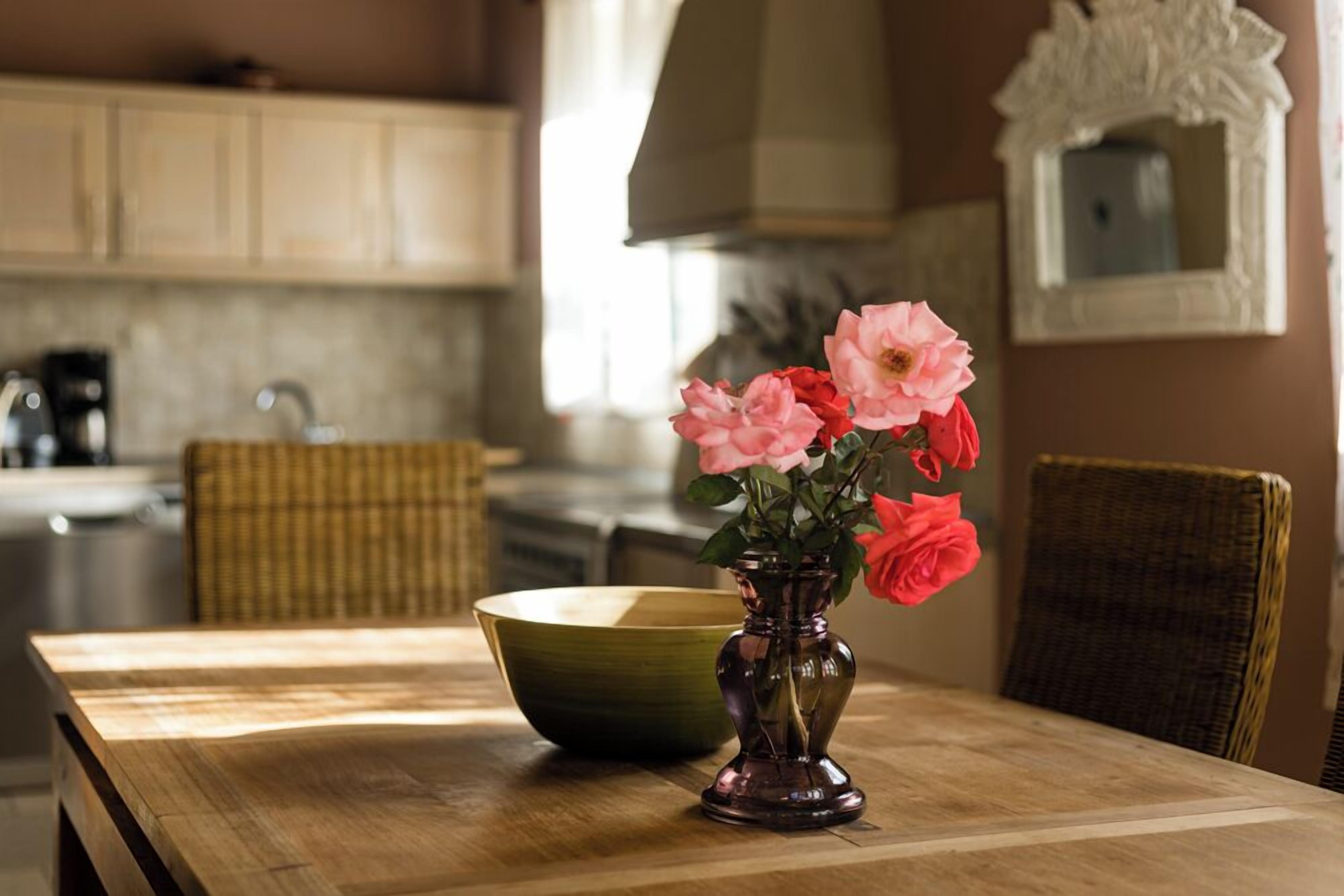 Una mesa de comedor de madera con un tazón verde y un florero oscuro con flores rosadas y rojas.