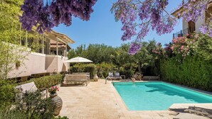 Ein Poolbereich mit gefliestem Deck, Liegestühlen und einer Pergola mit violetten Blumen.