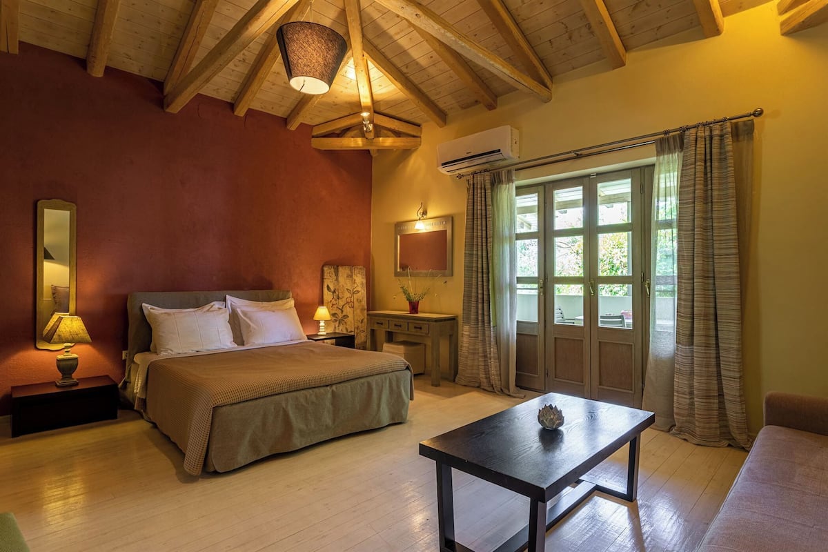 Une chambre à coucher comprenant un lit, une table de chevet, une lampe, un miroir, une commode et une fenêtre avec des rideaux.