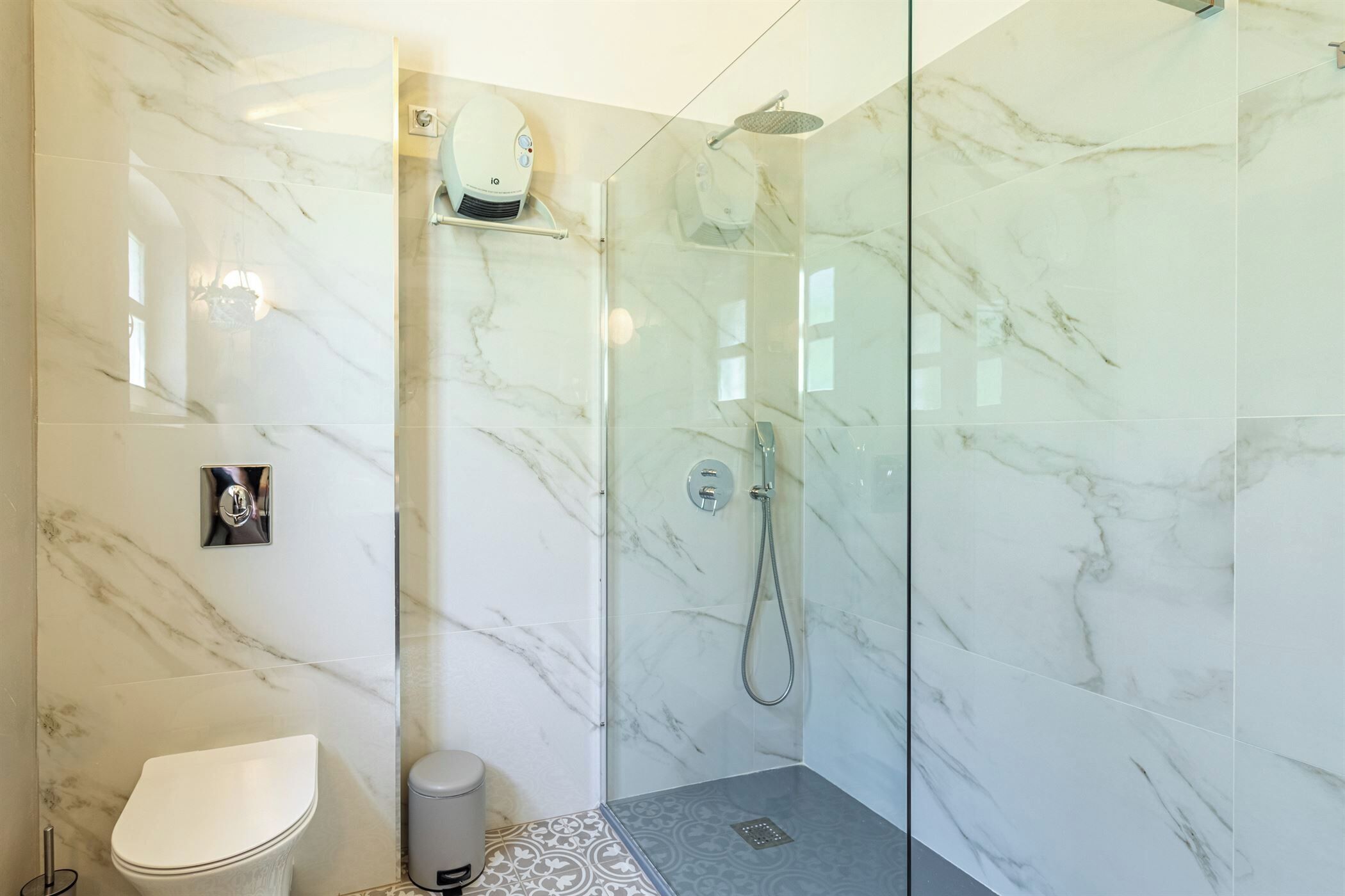A bathroom with a toilet, a shower with a glass door, and a marble wall.