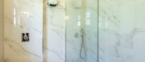 A bathroom with a toilet, a shower with a glass door, and a marble wall.