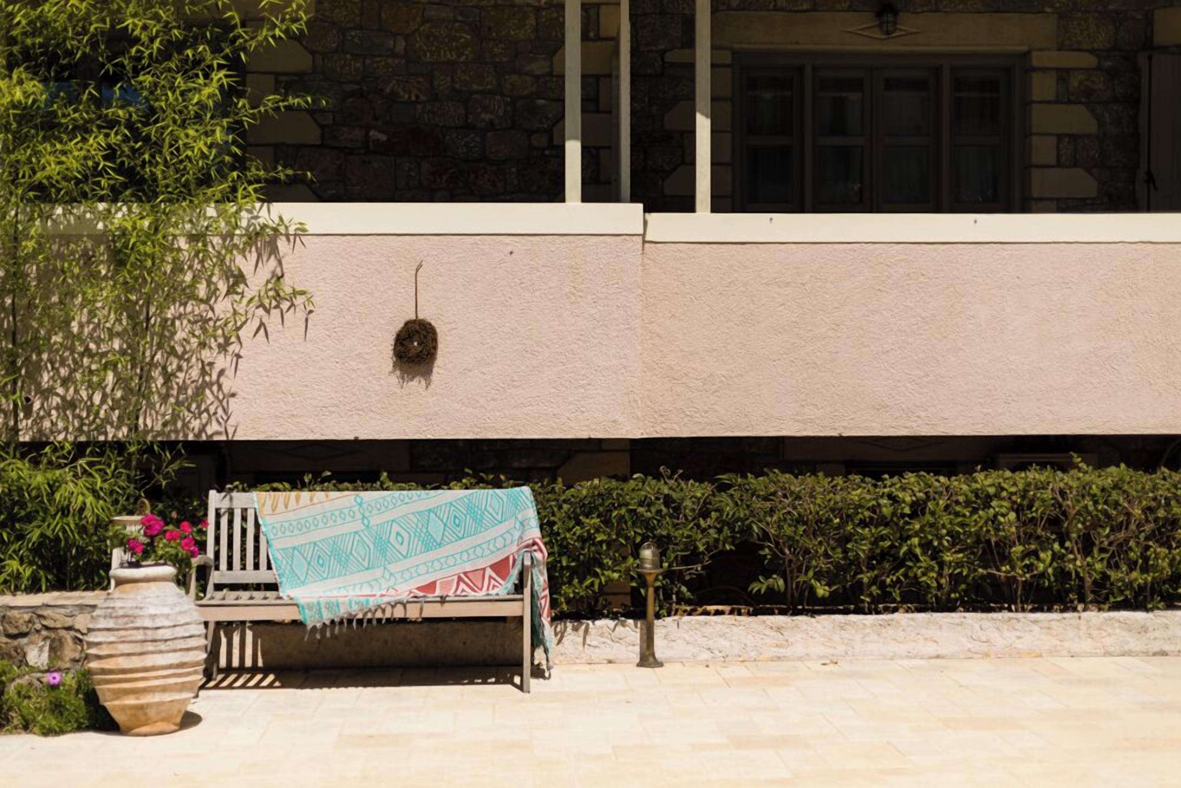 A stone building with a white exterior, a bench with a patterned blanket, and a potted plant with flowers.