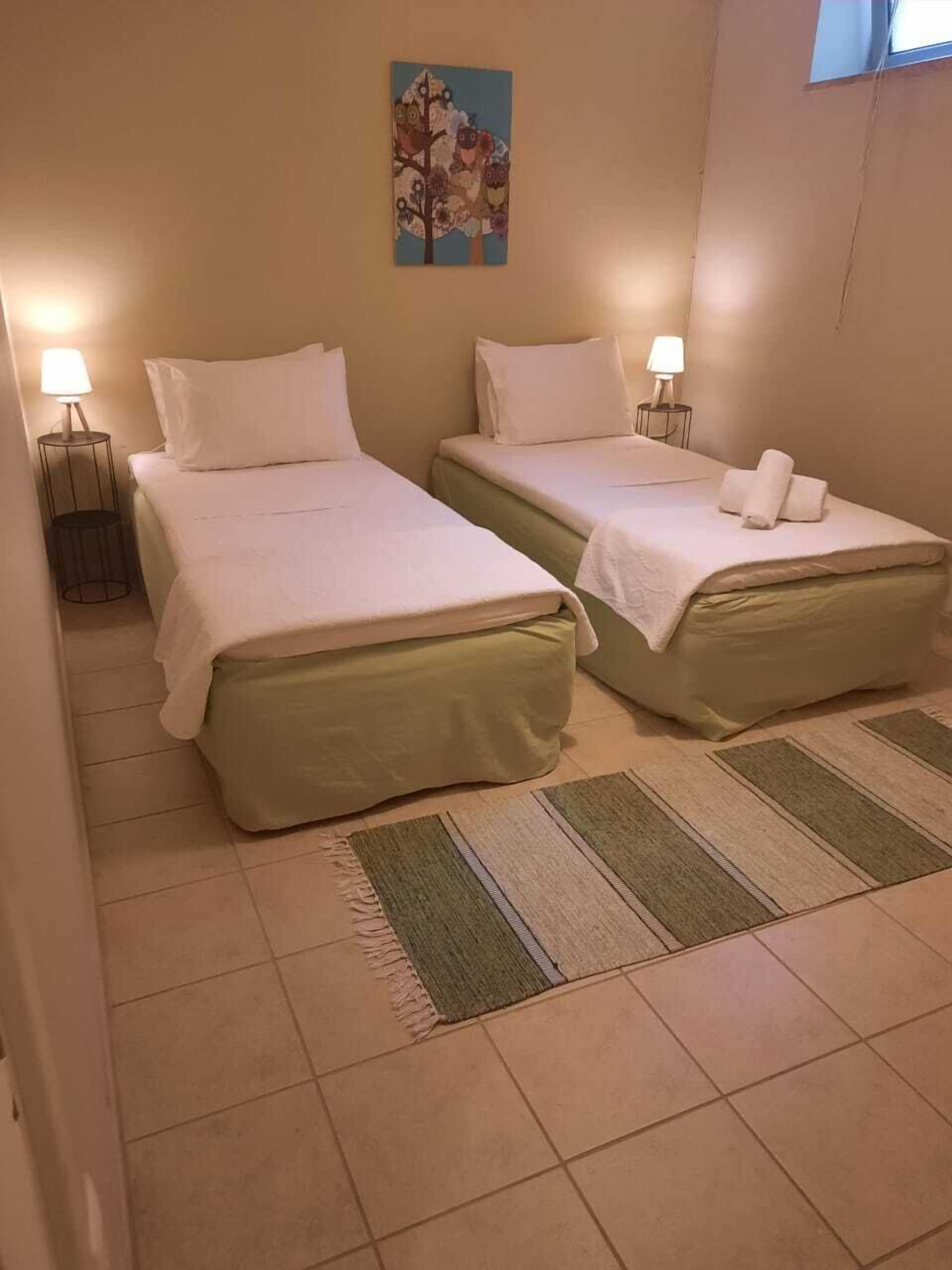 A hotel room with two beds, a small painting on the wall, and a window.