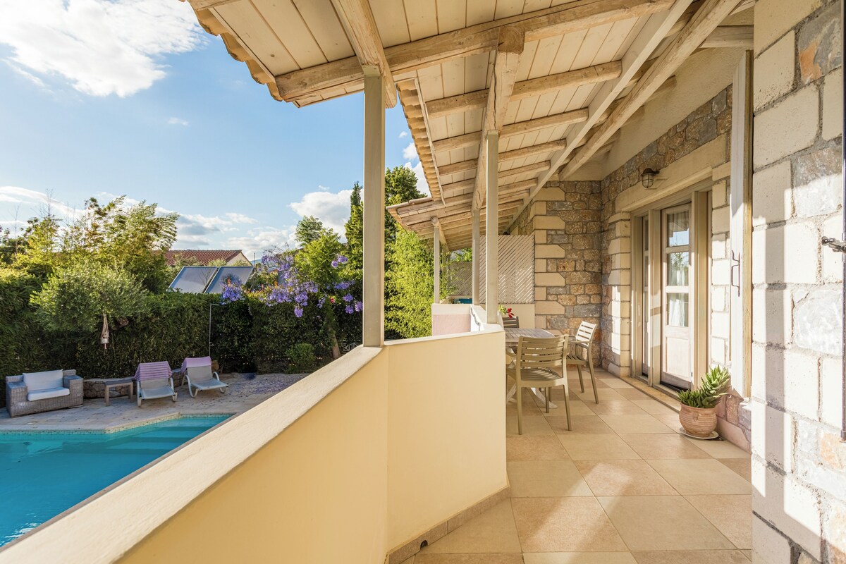 A covered patio with a pool, outdoor seating, and a stone wall.