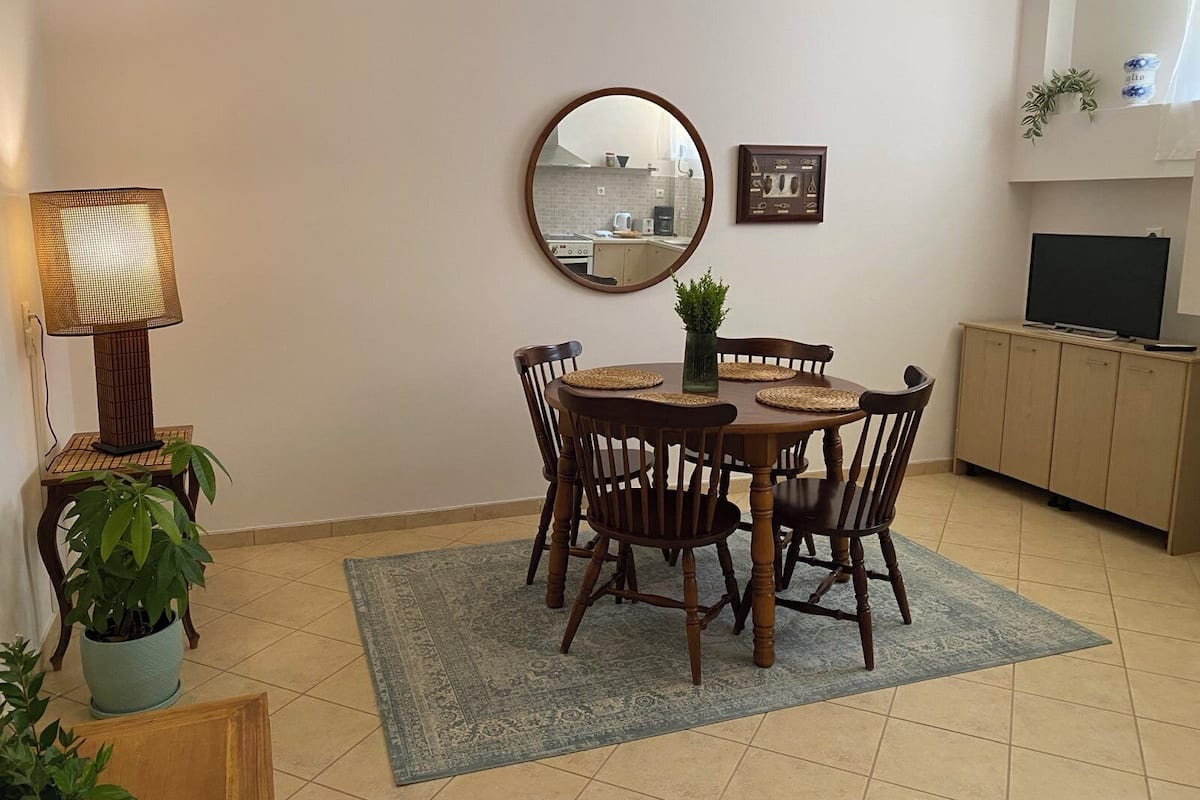 Un coin repas comprenant une table ronde, six chaises, un miroir, une lampe, un tableau encadré, un téléviseur et un meuble.